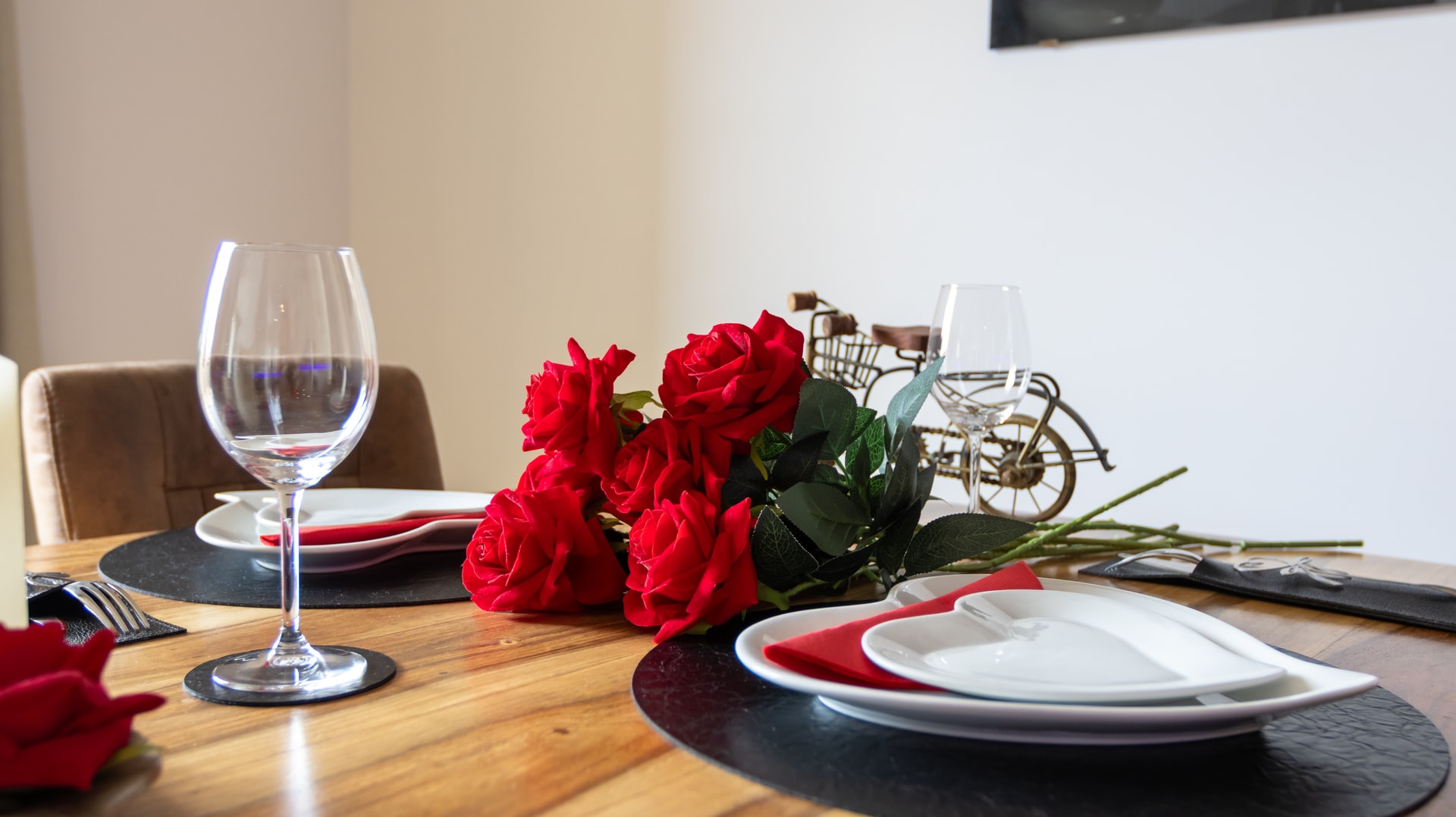 Table dressée pour deux : verres à vin, assiettes blanches sur sets ardoise, bouquet de roses rouges au centre