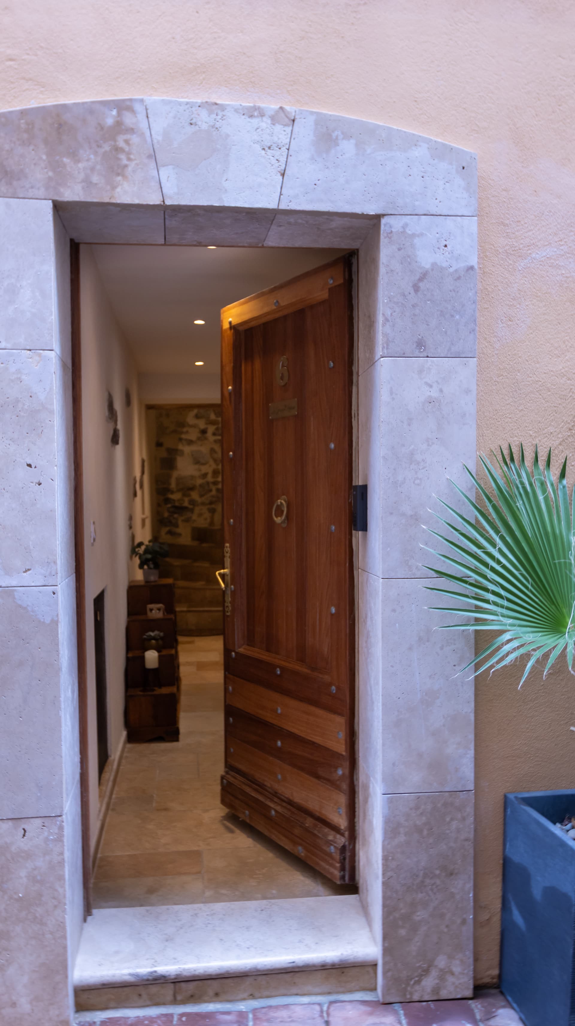 La porte d’entrée vue depuis la ruelle, encadrée par une arche de pierre, une plante en pot à droite