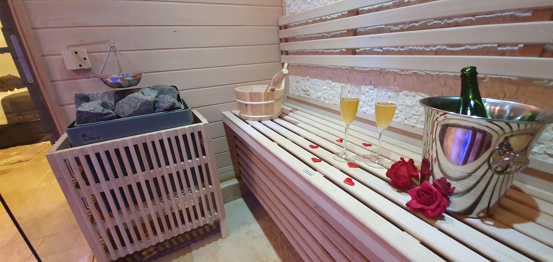 Le sauna en bois clair, son banc, un seau à champagne, deux verres et des pétales rouges posés sur le banc