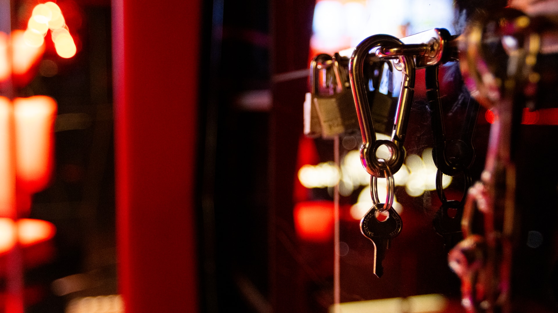 Gros plan sur des accessoires métalliques suspendus — mousqueton, cadenas — sous une lumière rouge
